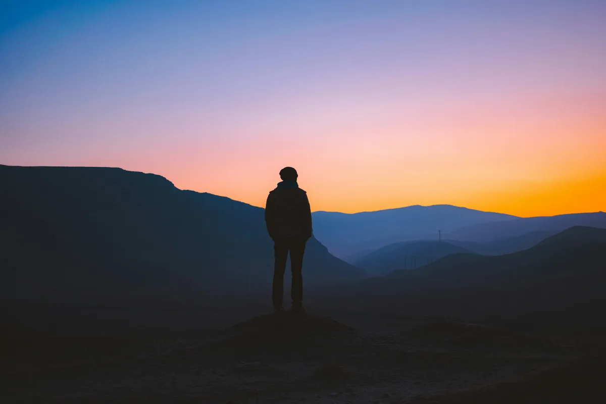 silhouette of man standing on mountain during sunset